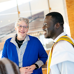 A woman in a blue sweater and glasses converses with a man in a white shirt.