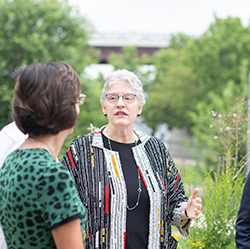 A group of people talking outdoors with trees and structures in the background.