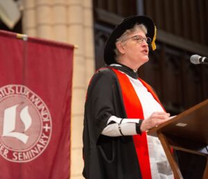 Wearing academic robes, Robin Steinke speaks at the 2025 Luther Seminary commencement.
