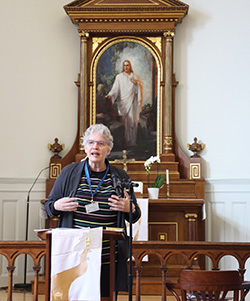 Robin Steinke gesturing while speaking at a podium inside a church in front of a religious painting.