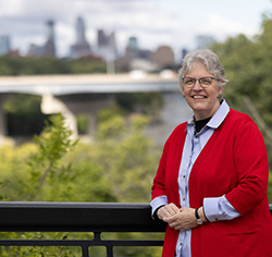 Portrait of Robin Steinke smiling in a red cardigan with a city skyline blurred in the background.