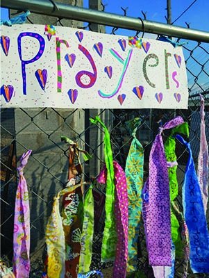 Pieces of colorful fabric tied to a fence under a sign that reads prayers