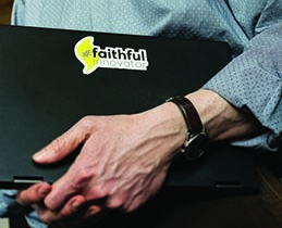 Person hodling laptop with Faithful Innovation sticker