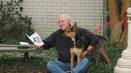 Person sitting with a German Shepherd dog, reading a booklet in a garden area with brick walls and greenery.