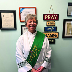 Person in a white robe with a green sash, standing in front of a wall displaying plaques and certificates.