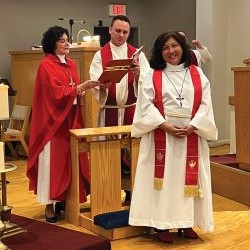 Three people in religious vestments stand inside a church near a pulpit.