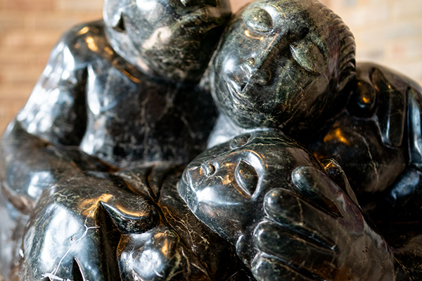 Close-up of a polished dark stone sculpture with three carved human faces showing serene expressions.