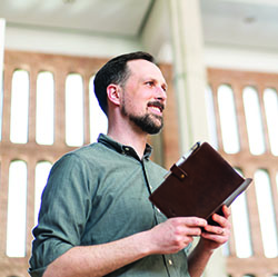 A man in a bright church, smiling while looking at a book.