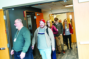 A group of people smiling and talking walk through an open doorway into a classroom or meeting room.