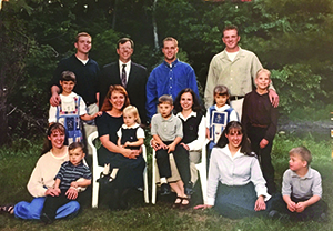 A large family group of adults, teenagers, and young children posing for a portrait outdoors in front of a background of dense green trees.